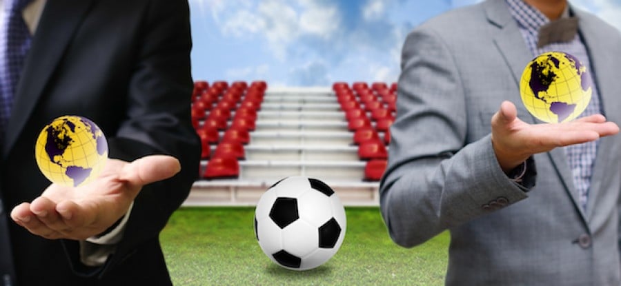 Global football with businessman holding small globes with football in between Global football with businessman holding small globes with football in between